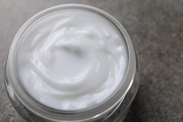 Face cream in jar on grey textured table, closeup