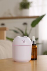Aroma diffuser and bottle of essential oil on wooden table at home