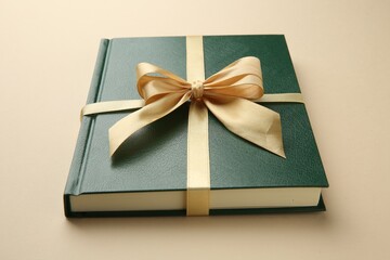 Book tied with golden ribbon on beige background, closeup. Perfect gift