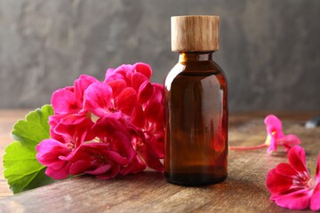 Geranium essential oil in bottle and beautiful flowers on wooden table