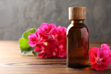 Geranium essential oil in bottle and beautiful flowers on wooden table