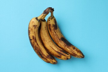 Bunch of ripe bananas with dark spots on light blue background, top view