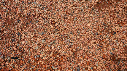 A close-up view of a red gravel surface, showcasing the varied shapes and sizes of the pebbles creates a unique pattern Background. Commonly used as a running track and other sports activities.