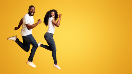 Playful Black Couple Running In The Air, having fun on yellow background
