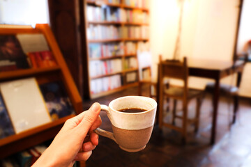 Hand holding cup of coffee in a bookstore, with books and table background