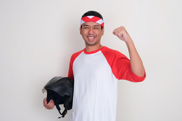 Indonesian man clenched fist and showing happy expression while holding motorcycle helmet