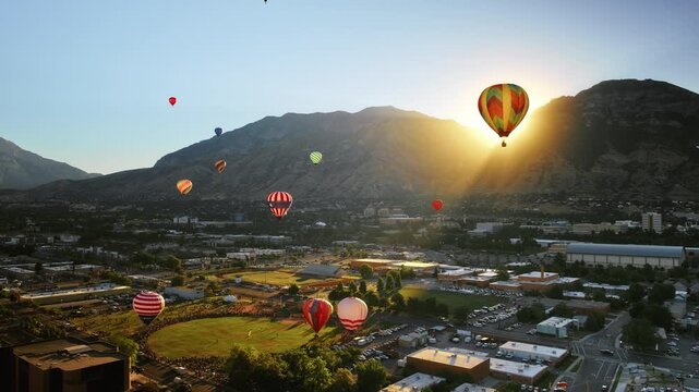 Majestic hot air balloons with sunrise over rocky mountains - wide, drone shot