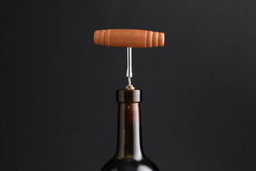 Wine bottle with corkscrew on dark background, closeup