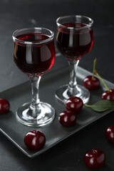 Delicious cherry liqueur in glasses and berries on black table, closeup