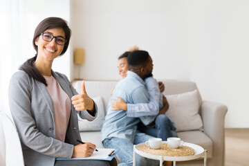 Successful Therapy. Psychologist Gesturing Thumb Up While Happy African American Spouses Hugging On Couch. Selective Focus, Copy Space