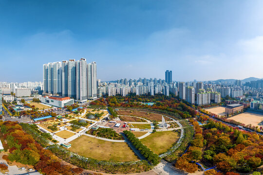 Jung-dong, Bucheon-si, Gyeonggi-do, South Korea - October 22, 2022: Aerial and autumnal view of trail and maple trees on Bucheon Central Park against apartments
