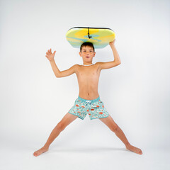 Young male beach boy in swim trunks, having fun doing the splits with his boogie board balanced on...