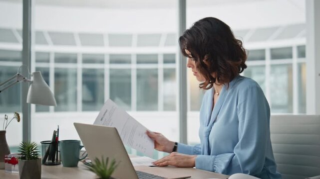 Focused accountant working laptop at desk office handling documents closeup.