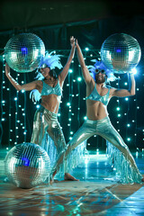 Disco Fever: A vibrant and energetic performance by a duo of dancers in shimmering silver costumes and feathered headwear, illuminated by a cascade of twinkling lights and disco balls