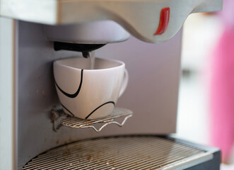 The coffee cup is being placed on the automatic coffee maker.