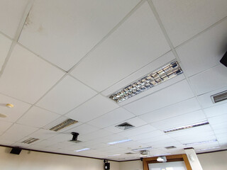 Office ceiling with white acoustic panels, fluorescent lights, air vents, and signs of water...