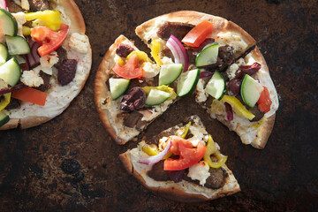 Greek Gyro Pita Pizza with Beef and Lamb Slices, Kalamata Olives, Feta and Veggies on a rustic baking sheet