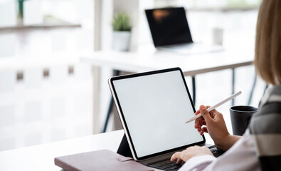 Mockup image of a woman holding stylus pen and using digital tablet with blank white desktop screen...
