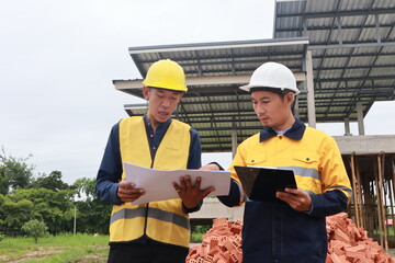 A male engineer, wearing a hardhat and helmet, examines blueprints on a construction site. Working...