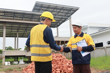 A male engineer, wearing a hardhat and helmet, examines blueprints on a construction site. Working as an architect and contractor, he oversees the development and renovation of buildings