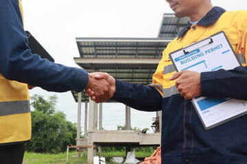 A male engineer, wearing a hardhat and helmet, examines blueprints on a construction site. Working...