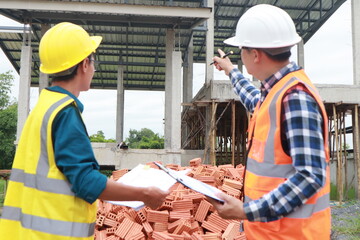 A male engineer, wearing a hardhat and helmet, examines blueprints on a construction site. Working...