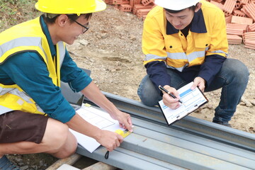 A male engineer, wearing a hardhat and helmet, examines blueprints on a construction site. Working...
