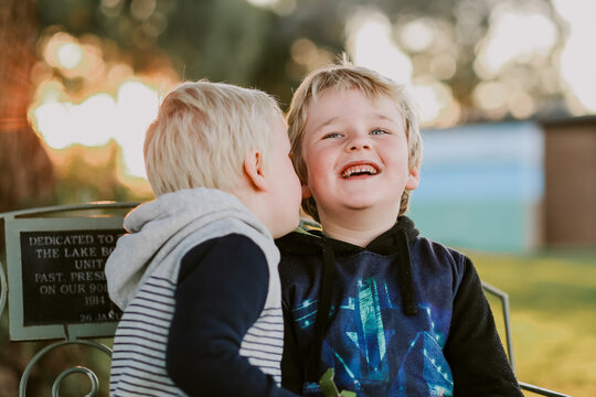 Two little boys sitting in garden setting at sunset telling secrets and laughing