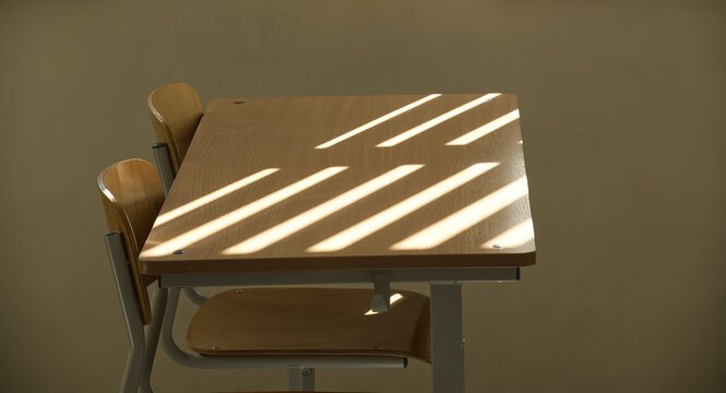 Empty classroom with wooden desks and sunlight casting shadow lines