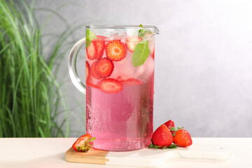 Freshly made strawberry lemonade with mint in jug and glass on white wooden table against grey background