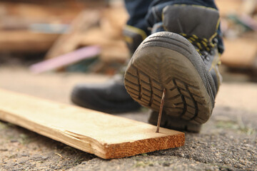 Careless worker stepping on nail in wooden plank outdoors, closeup