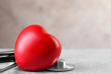 Fototapeta premium Stethoscope and red heart on grey stone table, closeup. Space for text