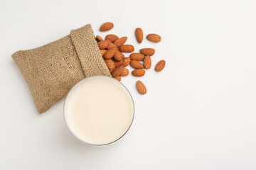 Fresh almond milk in glass, nuts and burlap sack on white background, top view. Space for text