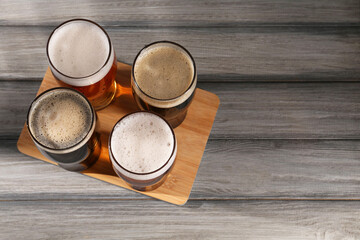 Glasses with different types of beer on grey wooden table, top view. Space for text