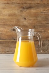 Tasty orange juice in jug on light wooden table