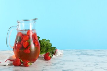 Tasty strawberry lemonade with mint in jug and berries on white marble table against light blue background. Space for text