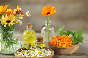 Different flowers, mint and bottles of essential oils on wooden table