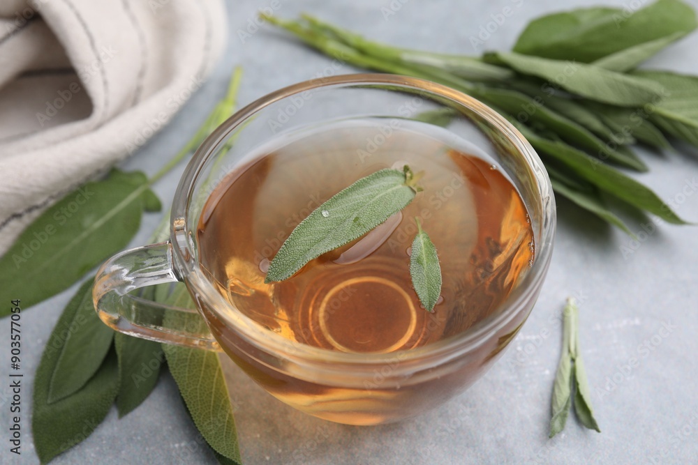 Sticker Aromatic herbal tea in cup with sage on grey table, closeup