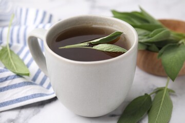 Aromatic herbal tea in cup with sage on white table, closeup