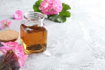 Bottle of geranium essential oil and beautiful flowers on light grey textured table
