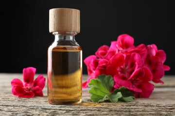 Bottle of geranium essential oil and beautiful flowers on wooden table, closeup