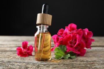 Bottle of geranium essential oil and beautiful flowers on wooden table, closeup