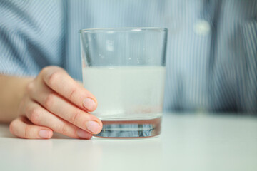 A woman drinks medicine: sits, holds a glass of water and a pill, expression of fatigue and discomfort