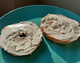 Plain bagel with cream cheese spread on teal plate in natural lighting 