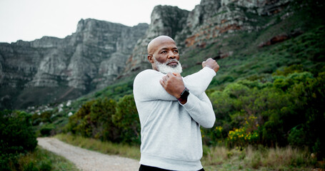 Runner, outdoor and senior black man stretching on road for fitness, health and running in retirement. Arms, exercise and male person in nature thinking of for workout, cardio warm up and training