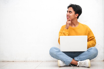 Asian young man sitting on the floor with his laptop doing thinking idea