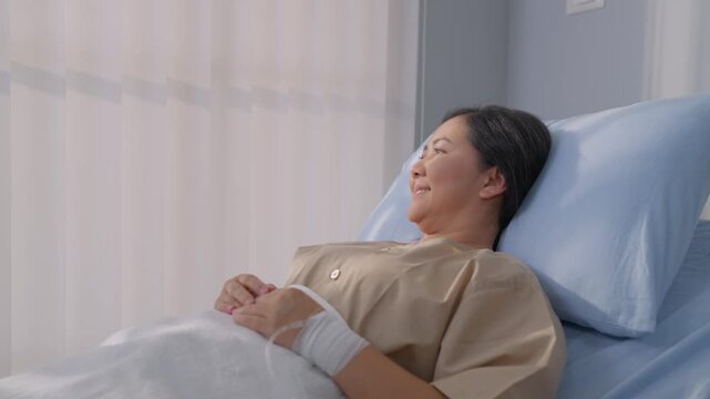 Asian mature female patient getting saline solution in hospital ward.