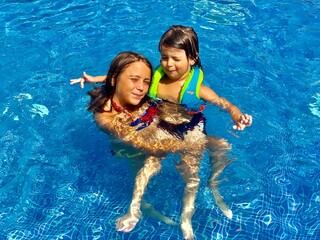 Two children happily swimming in a bright blue pool. They are enjoying the water, with one wearing...