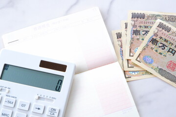 テーブルの上に開いた状態で置かれた銀行の預金通帳と、1万円札、電卓

