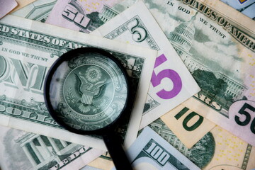 Big amount of US dollar bills in different nominations and magnifying glass. Many dollar banknotes...